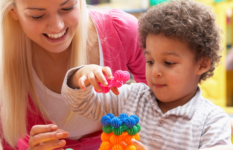 young woman stacking colorful blocks with curly-haired toddler boy